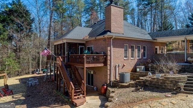 rear view of property featuring brick siding, a chimney, stairway, a sunroom, and cooling unit