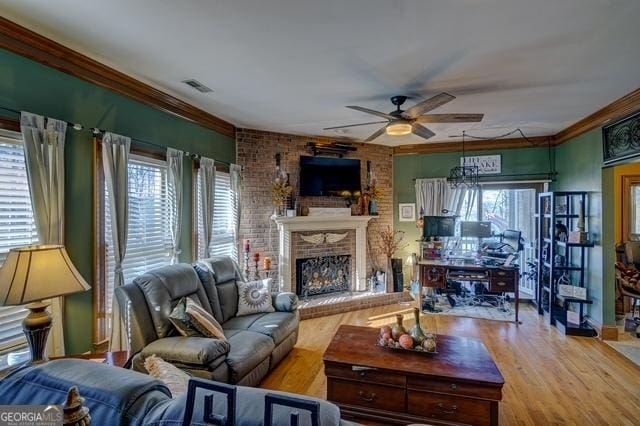 living area with visible vents, a ceiling fan, ornamental molding, wood finished floors, and a brick fireplace