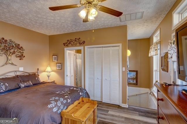 bedroom featuring a textured ceiling, wood finished floors, visible vents, and a ceiling fan