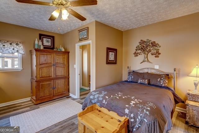 bedroom with ceiling fan, a textured ceiling, baseboards, and wood finished floors