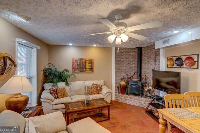 living area featuring a ceiling fan, a wood stove, visible vents, and a textured ceiling