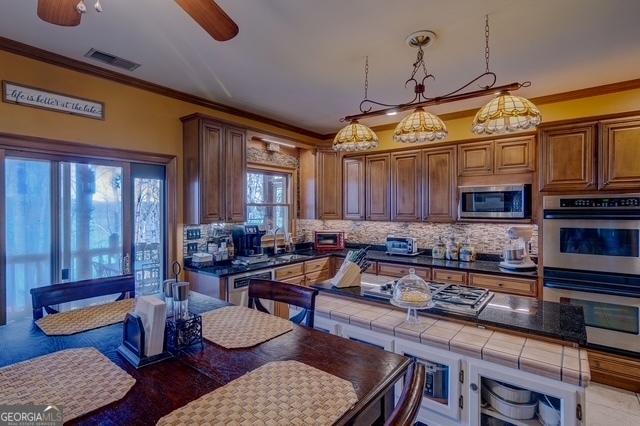 kitchen with stainless steel appliances, tasteful backsplash, visible vents, a ceiling fan, and ornamental molding