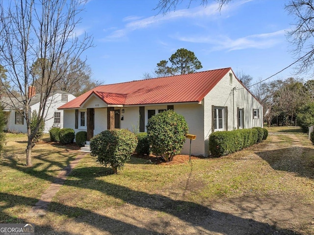 view of front facade featuring brick siding, metal roof, and a front yard