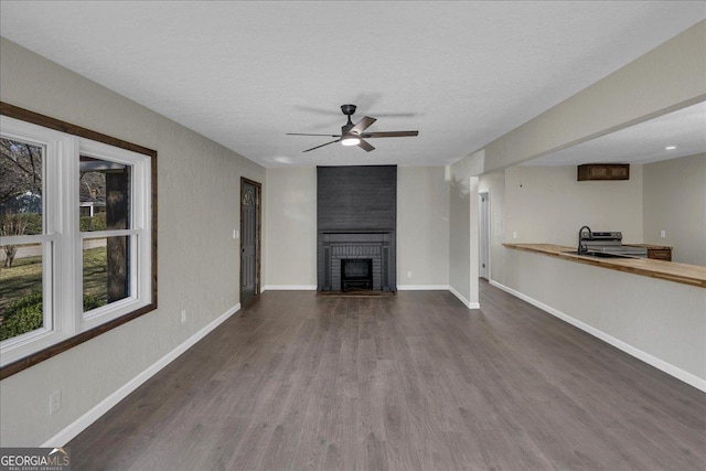 unfurnished living room with baseboards, dark wood finished floors, ceiling fan, a fireplace, and a sink