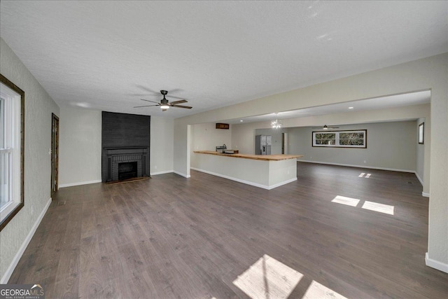 unfurnished living room featuring ceiling fan, dark wood-type flooring, a brick fireplace, and baseboards