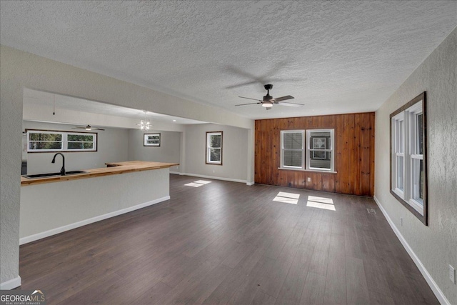 unfurnished living room featuring a textured ceiling, a sink, a ceiling fan, baseboards, and dark wood finished floors