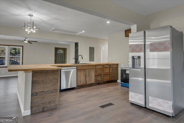 kitchen featuring dark wood-type flooring, a sink, baseboards, appliances with stainless steel finishes, and brown cabinetry