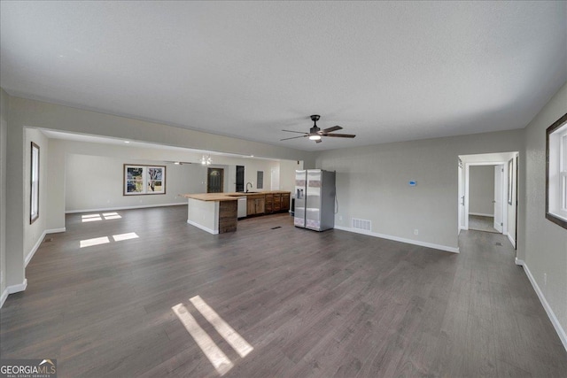 unfurnished living room featuring dark wood-style floors, visible vents, a sink, a textured ceiling, and baseboards