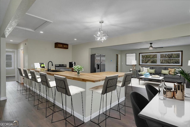 kitchen with dark wood-style floors, butcher block countertops, appliances with stainless steel finishes, a kitchen breakfast bar, and a sink