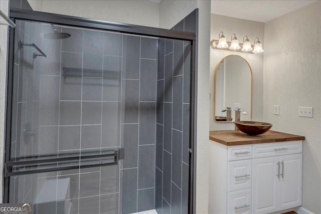 full bathroom with a textured wall, a shower stall, and vanity