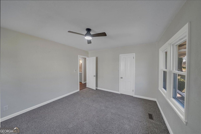 unfurnished bedroom with a ceiling fan, visible vents, dark carpet, and baseboards