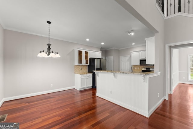 kitchen featuring light stone counters, a peninsula, appliances with stainless steel finishes, a kitchen bar, and dark wood finished floors