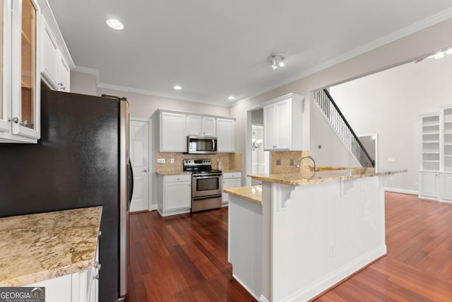 kitchen with white cabinets, appliances with stainless steel finishes, a kitchen breakfast bar, dark wood-type flooring, and a peninsula