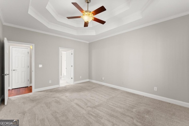 unfurnished bedroom featuring crown molding, a raised ceiling, ensuite bathroom, carpet flooring, and baseboards