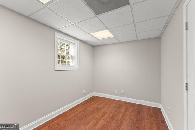 empty room featuring a paneled ceiling, baseboards, and wood finished floors