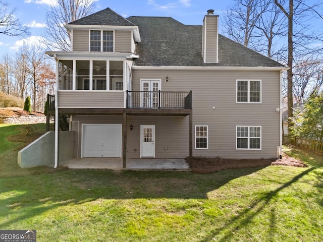 rear view of house with a yard, a chimney, a patio, an attached garage, and a sunroom