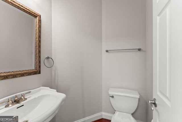 half bath with baseboards, a sink, and toilet