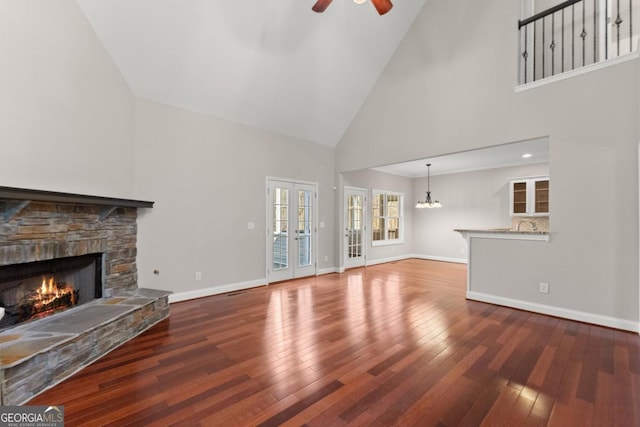 unfurnished living room featuring baseboards, a ceiling fan, wood-type flooring, a stone fireplace, and french doors