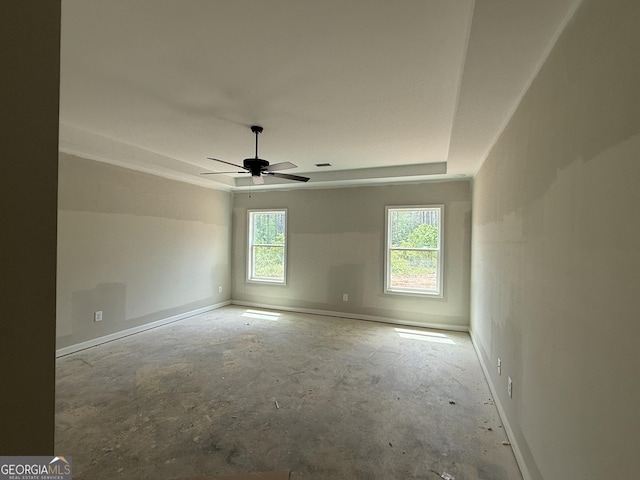 unfurnished room featuring unfinished concrete floors, a raised ceiling, baseboards, and a ceiling fan
