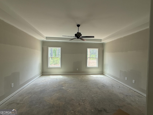 spare room with baseboards, a raised ceiling, ceiling fan, and unfinished concrete flooring