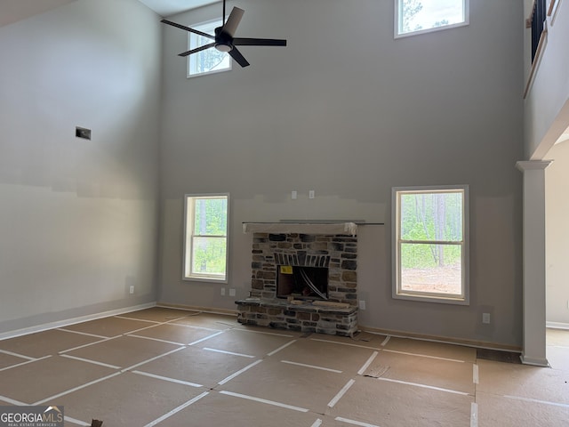 unfurnished living room with baseboards, a fireplace, a ceiling fan, and a high ceiling