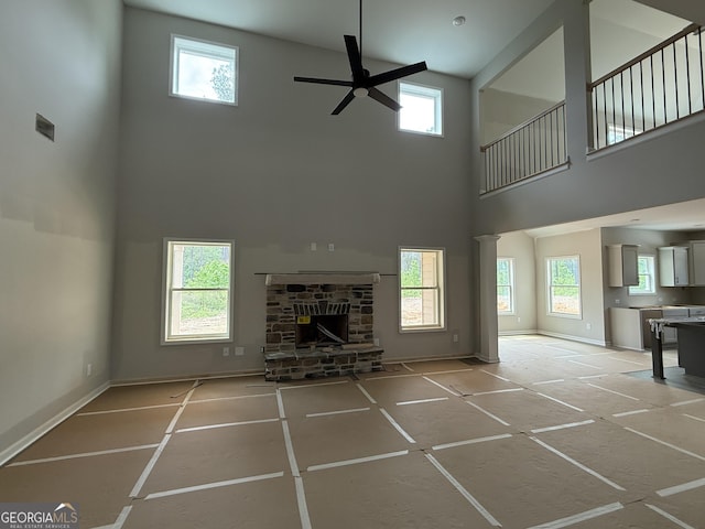 unfurnished living room with a towering ceiling, a wealth of natural light, a ceiling fan, and a stone fireplace