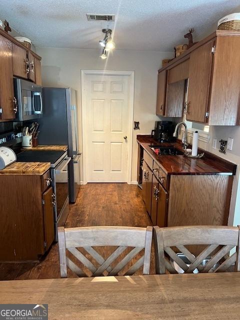 kitchen with dark wood-style flooring, dark countertops, stainless steel microwave, a sink, and range with electric cooktop