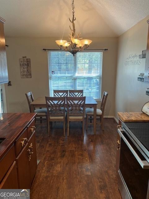 dining room with dark wood-style flooring, a notable chandelier, vaulted ceiling, and a textured ceiling