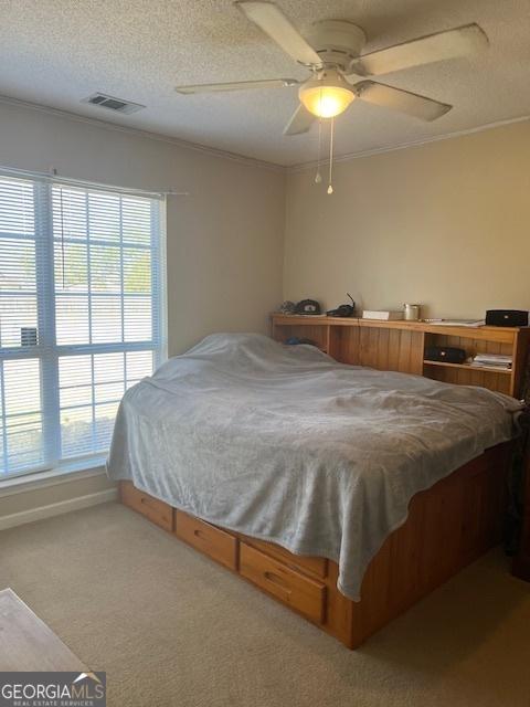 bedroom featuring visible vents, a ceiling fan, carpet, a textured ceiling, and crown molding