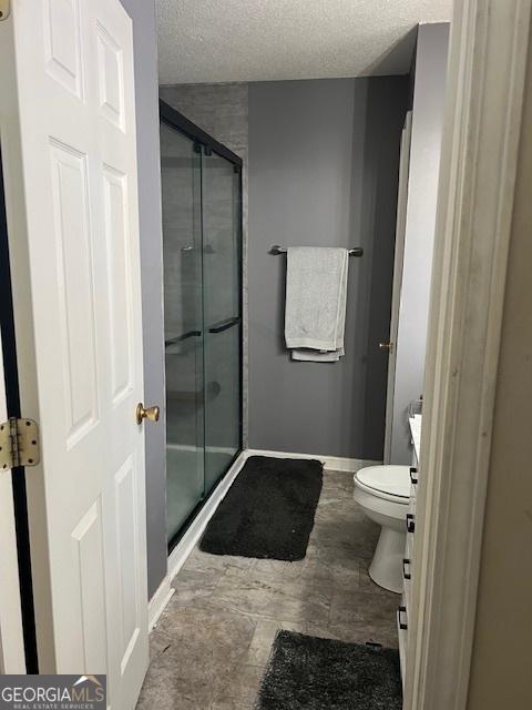 bathroom featuring toilet, a stall shower, a textured ceiling, vanity, and baseboards