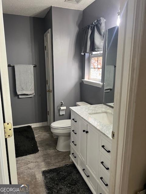 bathroom featuring a textured ceiling, toilet, visible vents, vanity, and baseboards