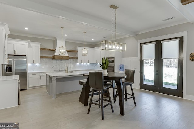 dining space with visible vents, beam ceiling, ornamental molding, french doors, and a decorative wall