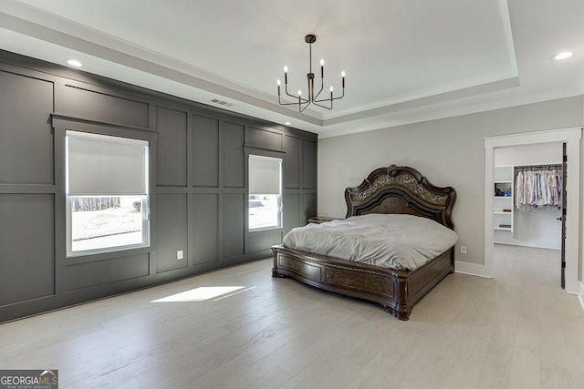 bedroom featuring light wood finished floors, a tray ceiling, crown molding, a decorative wall, and a chandelier