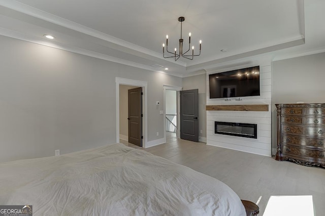 bedroom with a tray ceiling, a notable chandelier, wood finished floors, and a large fireplace