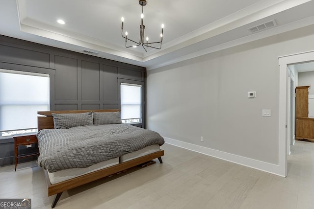 bedroom with visible vents, a chandelier, light wood-type flooring, a tray ceiling, and a decorative wall