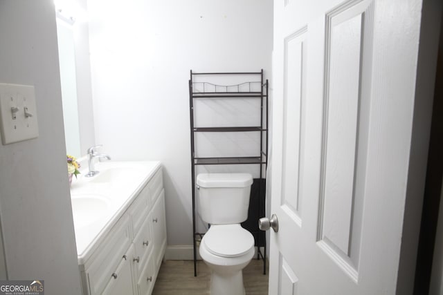 bathroom featuring double vanity, toilet, a sink, wood finished floors, and baseboards