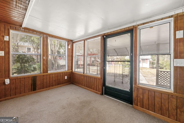 unfurnished sunroom with wood walls, vaulted ceiling, and carpet floors