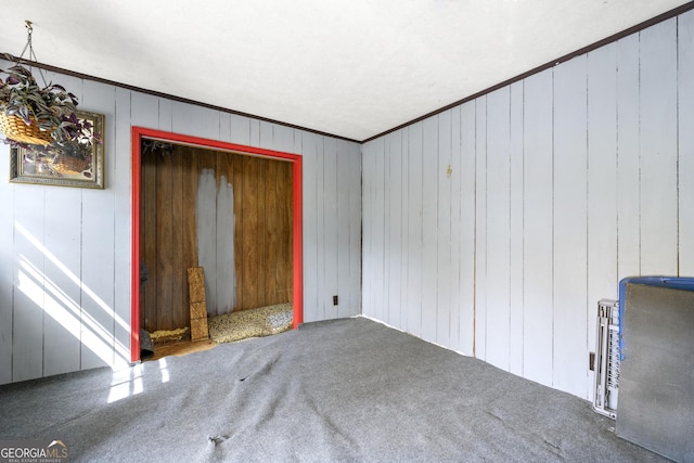 unfurnished living room featuring crown molding, wooden walls, and carpet