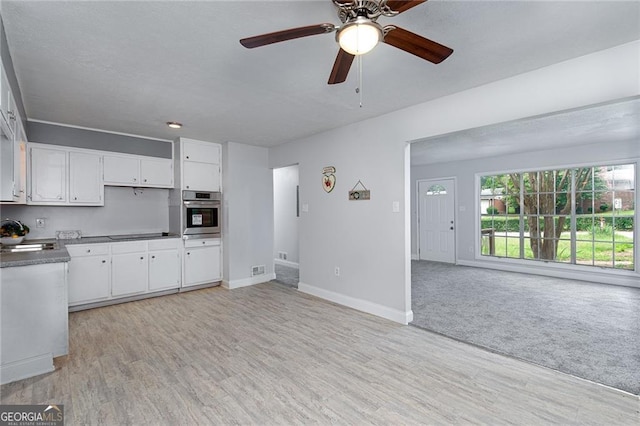 kitchen featuring white cabinetry, stainless steel oven, open floor plan, and light wood-style flooring