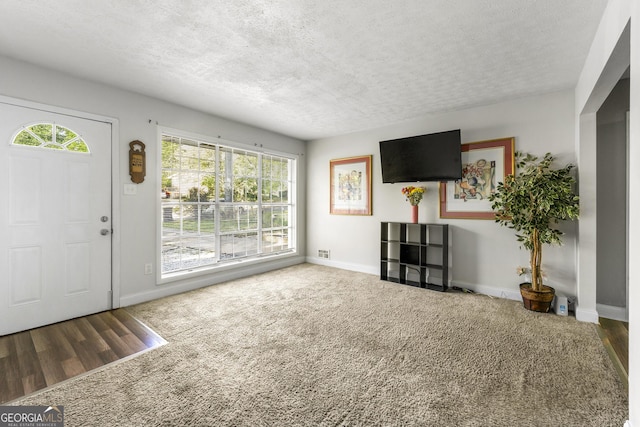 unfurnished living room featuring baseboards, wood finished floors, and a textured ceiling