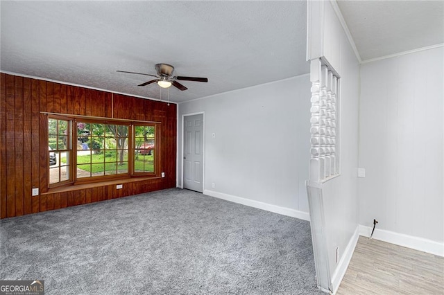 carpeted spare room with a textured ceiling, wooden walls, a ceiling fan, baseboards, and crown molding