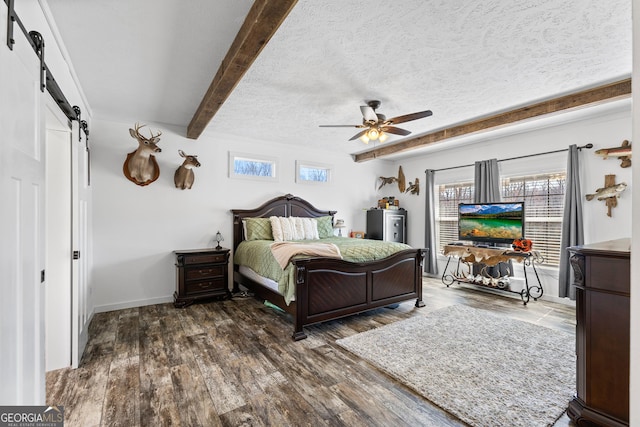 bedroom featuring beam ceiling, a barn door, a textured ceiling, wood finished floors, and baseboards