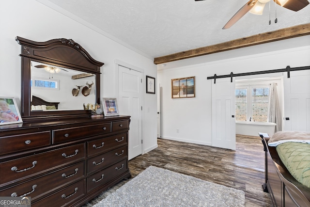 bedroom featuring a barn door, dark wood-type flooring, a ceiling fan, a textured ceiling, and baseboards