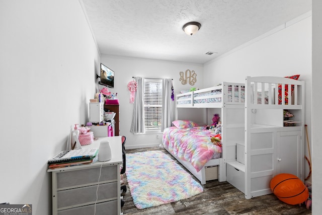 bedroom with a textured ceiling, wood finished floors, visible vents, and baseboards