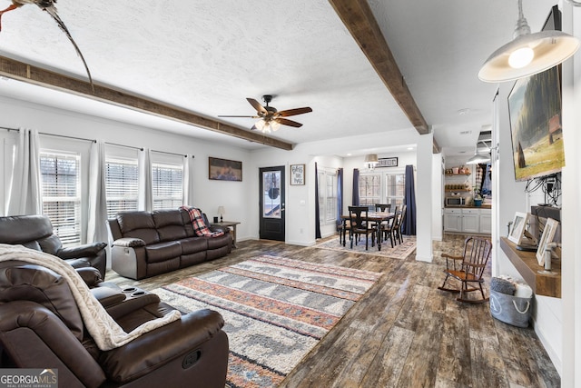 living area featuring beam ceiling, hardwood / wood-style floors, a ceiling fan, a textured ceiling, and baseboards