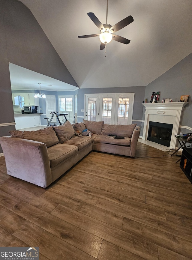 living area featuring a fireplace with flush hearth, dark wood-style flooring, high vaulted ceiling, and ceiling fan with notable chandelier