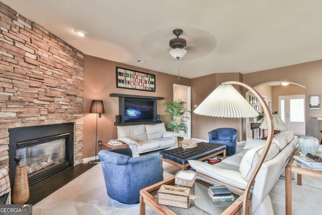 living area featuring baseboards, a fireplace, arched walkways, and a ceiling fan