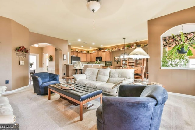 living room featuring light carpet, baseboards, arched walkways, and recessed lighting