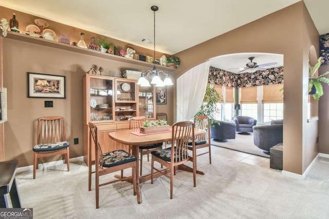 dining room with arched walkways, light carpet, vaulted ceiling, baseboards, and ceiling fan with notable chandelier