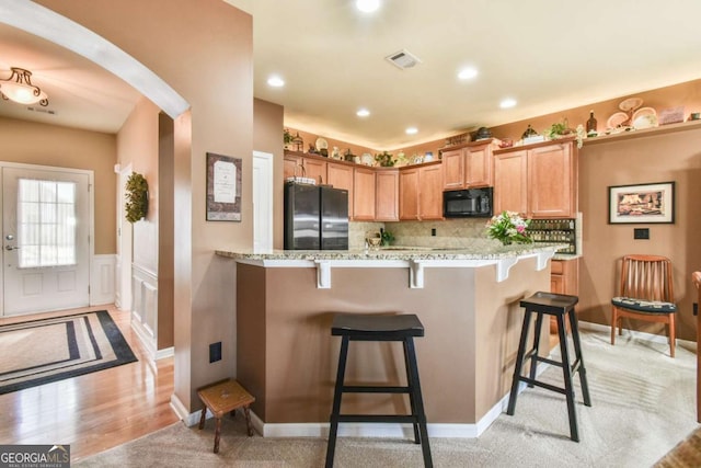 kitchen with black appliances, arched walkways, a breakfast bar, and light stone counters